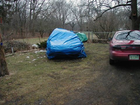 1997 Ford Taurus - A red 1997 Ford Taurus is parked next to a large blue tarp covering an unknown object.