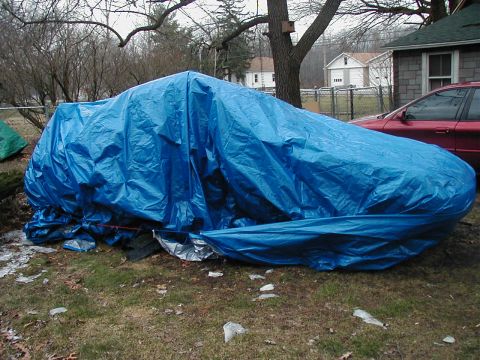 1997 Ford Taurus - A car is completely covered by a blue tarp, obscuring its make and model.