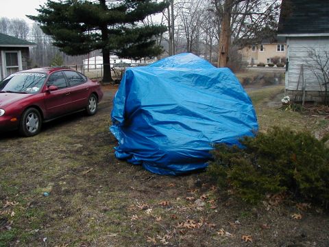 1997 Ford Taurus - A red sedan is parked next to a large object covered by a blue tarp in a yard.