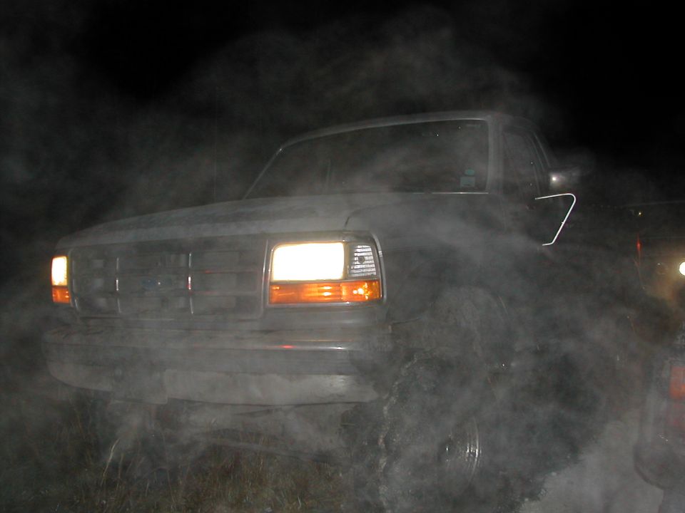 Ford Bronco front end at night lit by its headlights through heavy steam