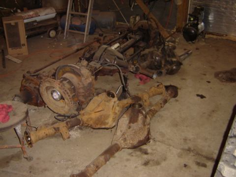 1992 Ford Bronco - Disassembled vehicle axles and differential parts are piled on a garage floor, showing significant rust and wear.