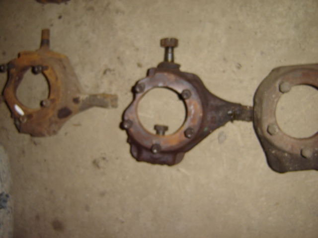 Two rusty metal steering knuckles with bolt holes on a concrete surface