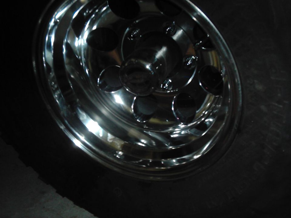 Chrome wheel with five large circular cutouts and a tire. Supermotors.net logo visible