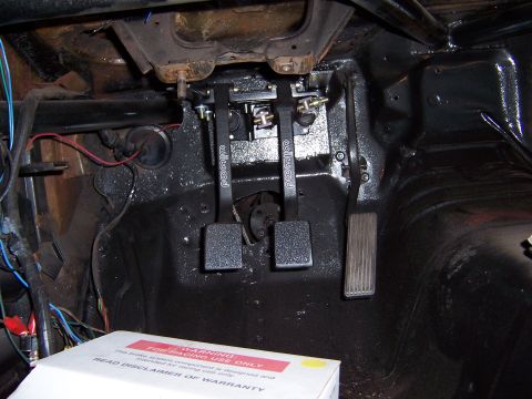 1971 Ford Mustang - Close-up of a car's interior, focusing on the brake and clutch pedals, with visible wiring and a warning label on a box.