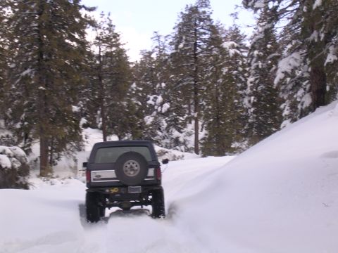 1999 Toyota Tacoma - A 1990s Ford Bronco navigates a snow-covered forest road, its rear end kicking up snow as it drives away.