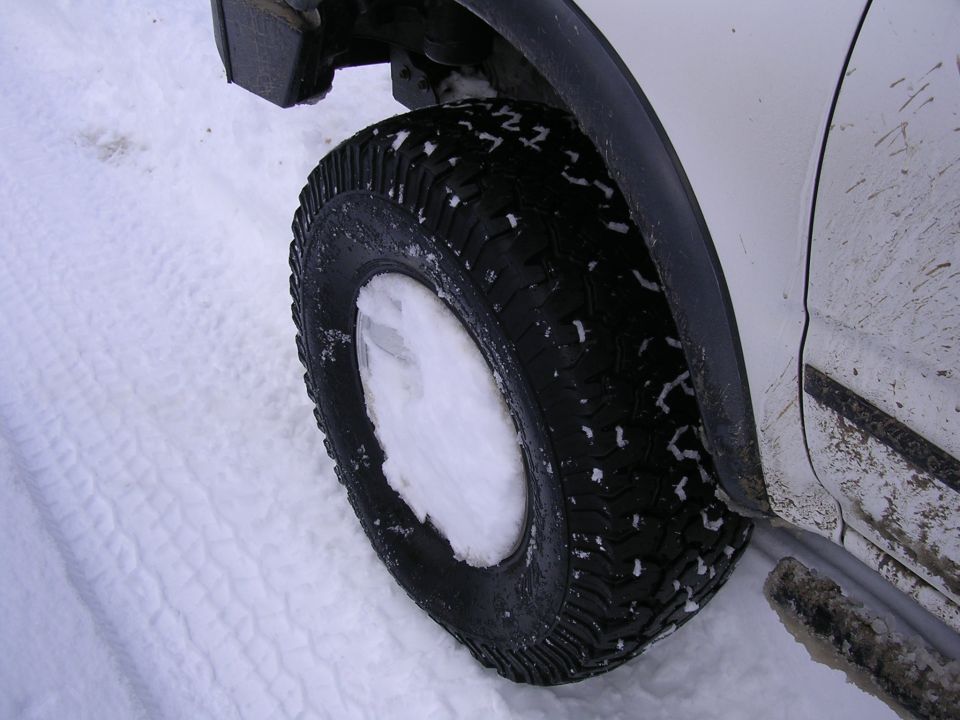 Close-up of a vehicle's tire and fender in the snow. White markings are visible on the tire