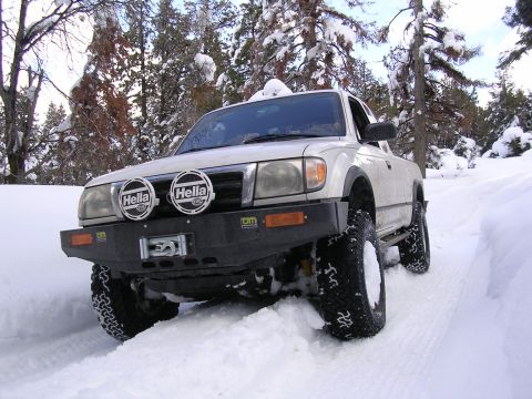 1999 Toyota Tacoma - A 1999 Toyota Tacoma navigates a snowy trail with aftermarket off-road lights and bumper.