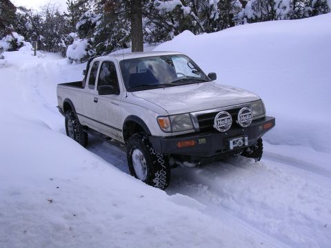 1999 Toyota Tacoma - A white Toyota pickup truck navigates a snowy road, its off-road tires gripping the snow-covered terrain.