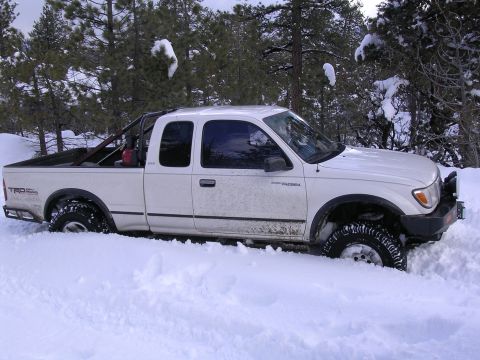 1999 Toyota Tacoma - A white 1999 Toyota Tacoma is stuck in deep snow, with only its tires and lower body visible.