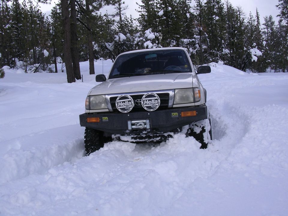1999 Toyota Tacoma driving through deep snow, front view with aftermarket bumper and Hella lights