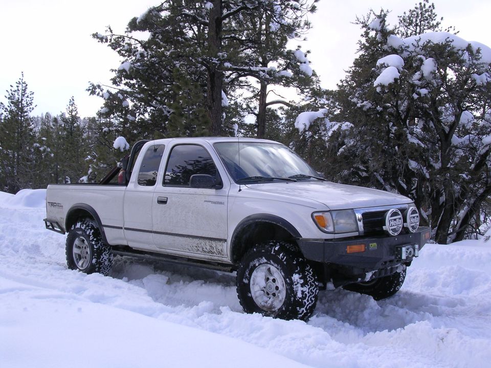 White 1999 Toyota Tacoma pickup truck driving in snow with aftermarket bumper and lights
