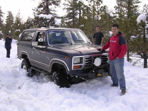 1999 Toyota Tacoma - A dark blue Ford Bronco is partially submerged in snow, with several people standing nearby.