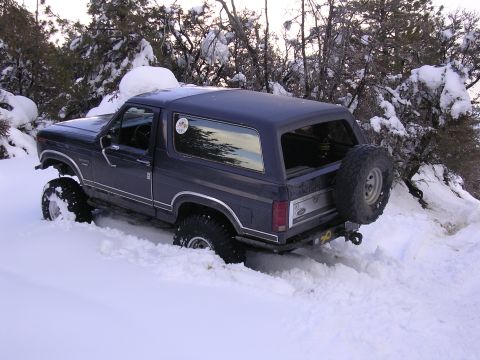 1999 Toyota Tacoma - Ford Bronco navigating deep snow off-road, showing its lifted suspension and rear-mounted spare tire.