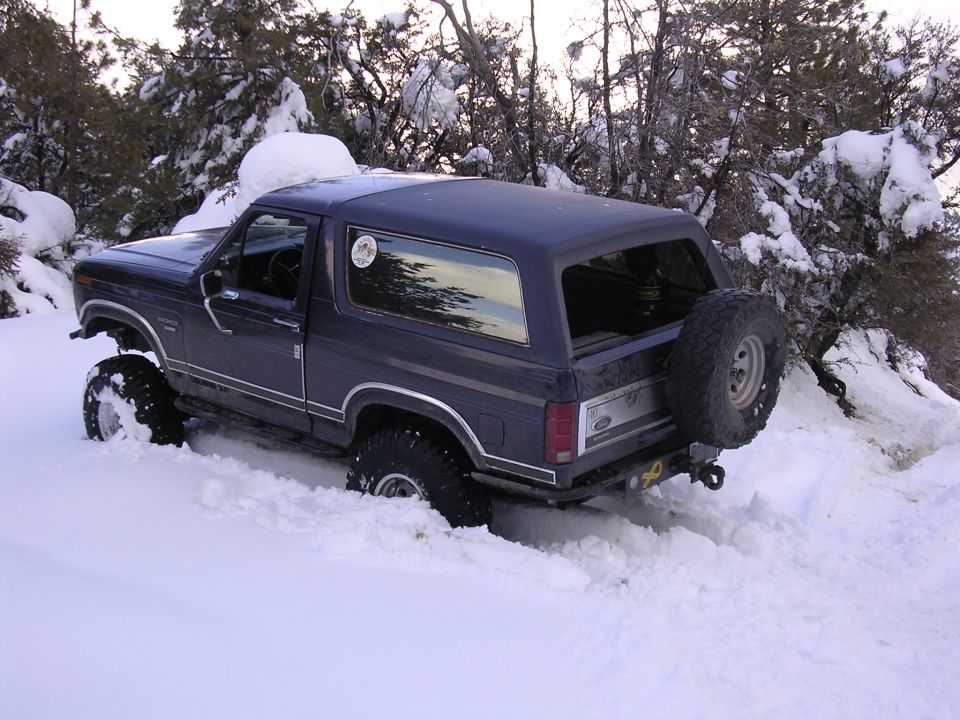 Dark blue Ford Bronco with lifted suspension stuck in deep snow, spare tire mounted on rear door