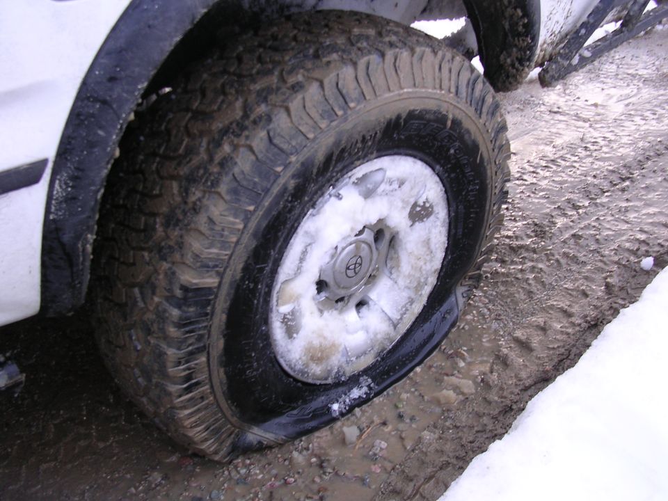 Flat tire on white truck with Toyota logo on hubcap, in snowy, muddy conditions
