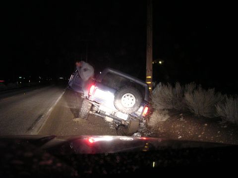 1999 Toyota Tacoma - A person stands by a vehicle that has gone off the road at night, leaning against a utility pole.