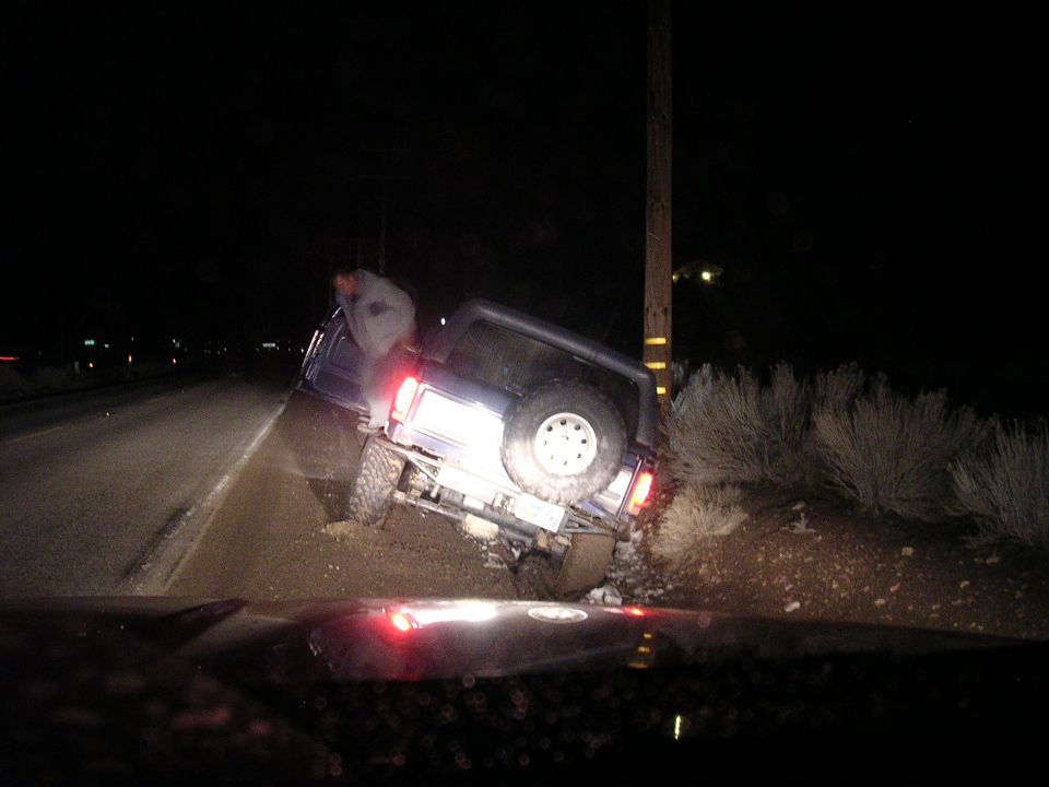 SUV is tilted off the road, with its rear tire on an embankment next to a utility pole