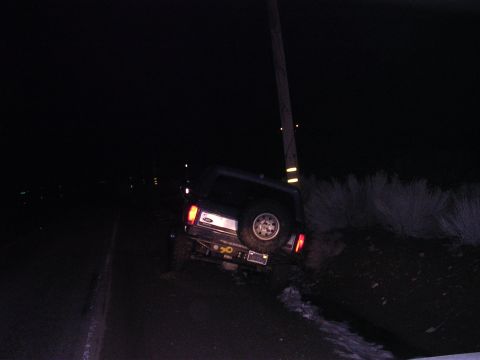 1999 Toyota Tacoma - A dark SUV is parked off the road at night, leaning against a utility pole with its spare tire visible on the rear.