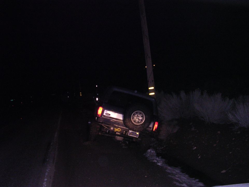 Dark SUV with spare tire on rear, off-road at night, leaning against a utility pole