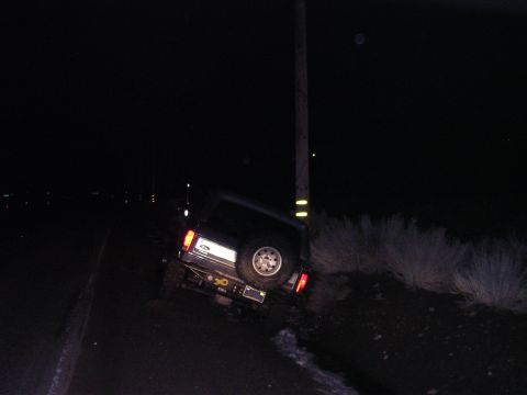 1999 Toyota Tacoma - A dark SUV is seen leaning against a utility pole at night, with its rear end visible and a spare tire mounted on the door.