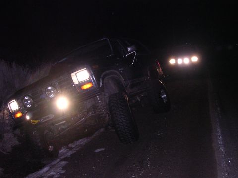 1999 Toyota Tacoma - A black off-road truck navigates a dark, uneven terrain at night, with another vehicle's lights illuminating the scene.
