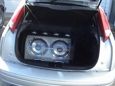 1994 Ford Bronco - The rear of a silver car shows an aftermarket dual subwoofer box installed in the trunk area.