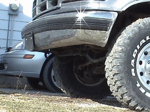 1994 Ford Bronco - Close-up of a truck's front bumper and tire, with a silver car visible behind it.