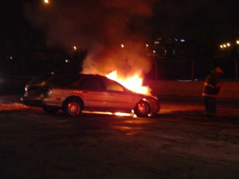 1979 Ford Bronco - A car is ablaze at night, with a firefighter observing the scene.
