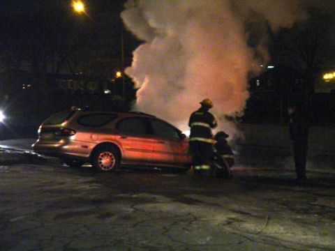 1979 Ford Bronco - Firefighters attend to a burning station wagon at night.