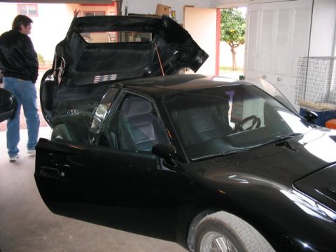 1993 Ford Taurus - A black coupe with its gullwing doors open is parked inside a garage, with a man standing to the left.