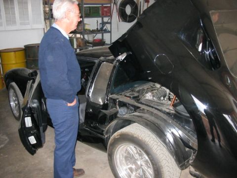 1993 Ford Taurus - A man inspects a black sports car with its hood and door open in a garage.