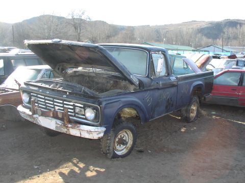 1981 Ford Bronco - This weathered Ford truck sits in a junkyard, its hood ajar, revealing a dusty engine bay.