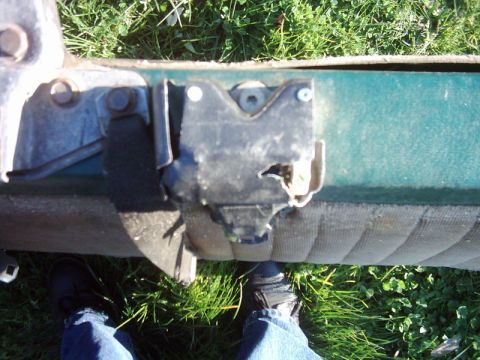1978 Ford Bronco - Close-up of a worn door latch mechanism on a green vehicle, with a person's feet visible in jeans and dark shoes.