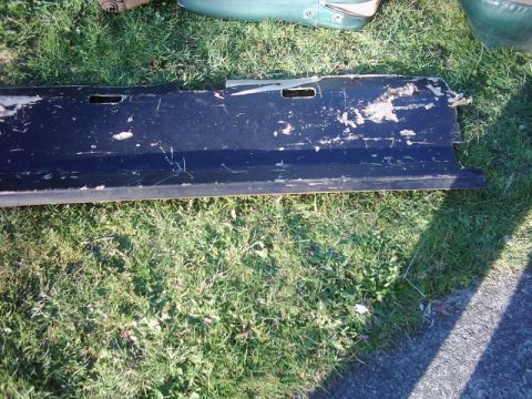 1978 Ford Bronco - A black tailgate, likely from a Ford Bronco, lies on the grass with significant paint damage and wear.