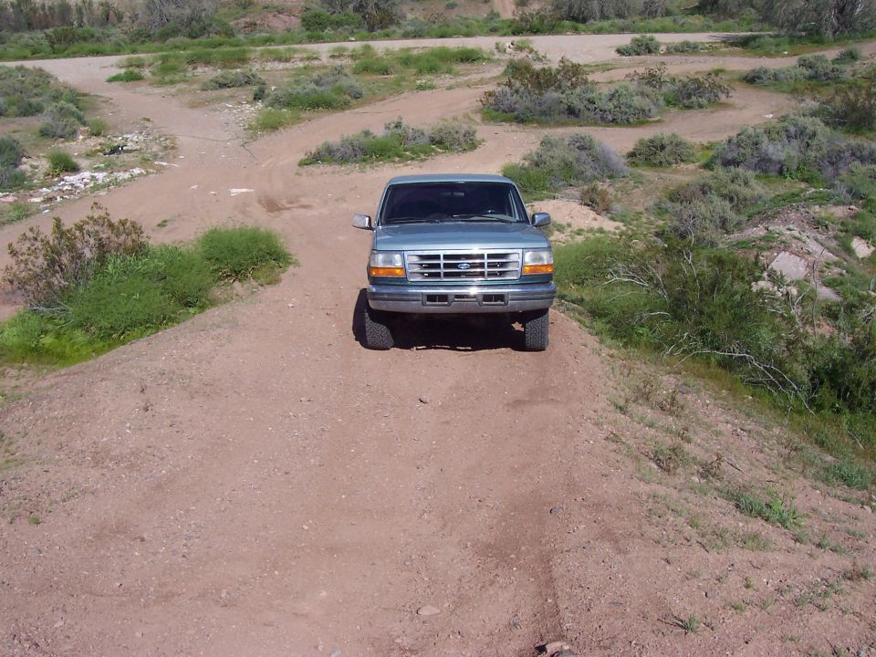 Light blue Ford F-series truck parked on a dirt wash trail in high desert scrub