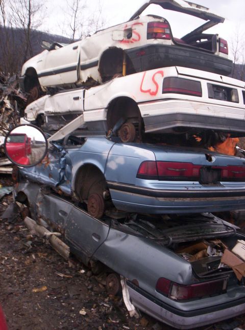 1971 Ford Mustang - Multiple vehicles are stacked in a junkyard, showing signs of significant damage and disrepair.