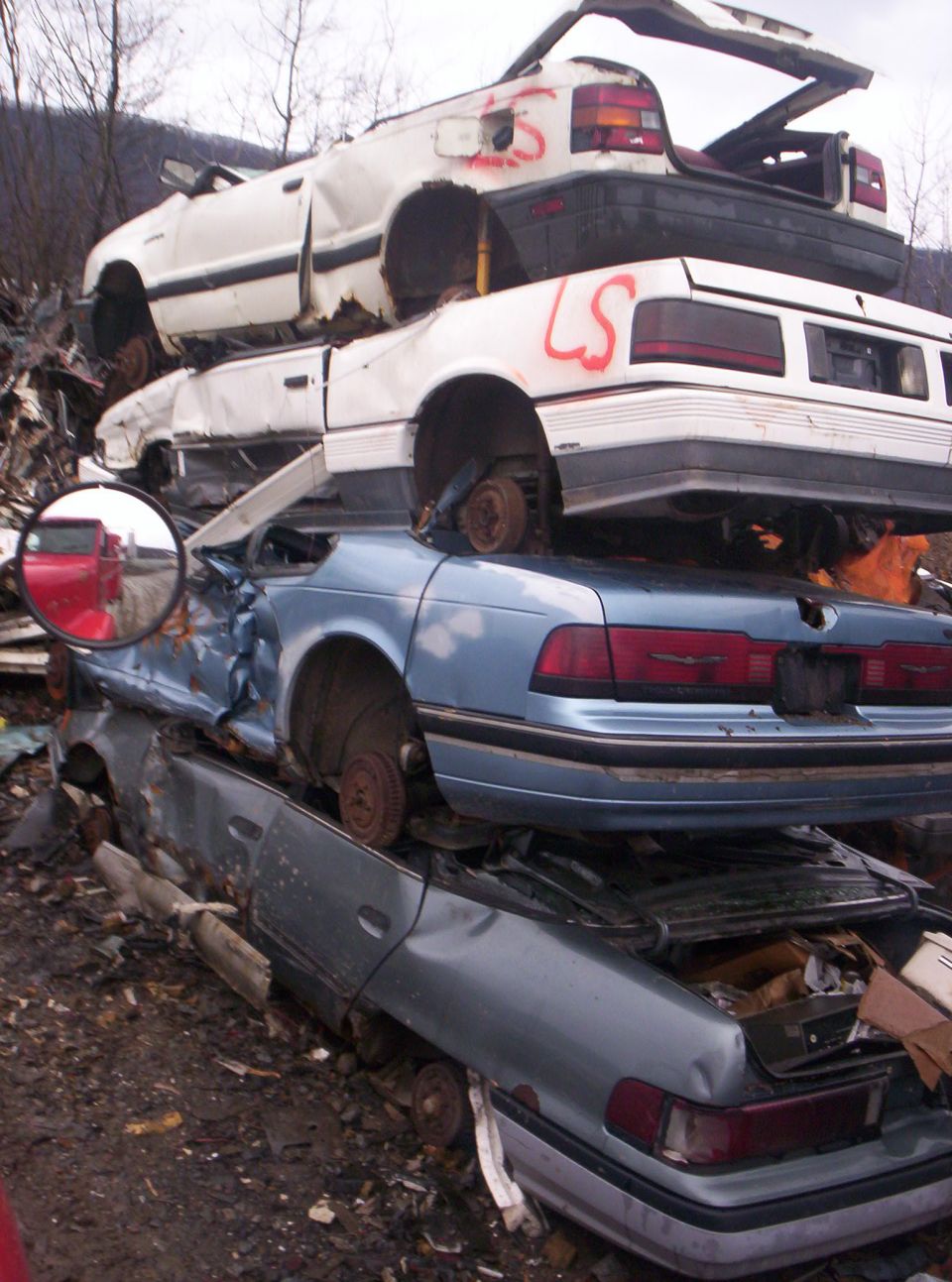 several wrecked cars piled up in a junkyard, one is blue, two are white