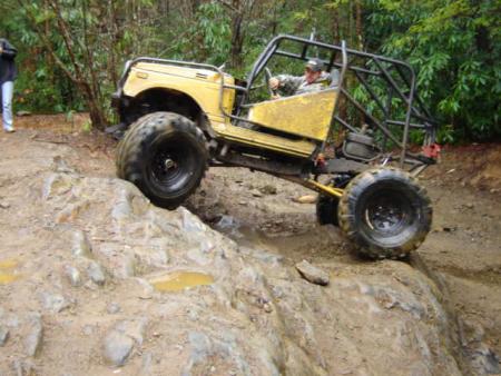 1989 Ford Bronco - A modified yellow off-road vehicle navigates a rocky and muddy trail with a driver inside.