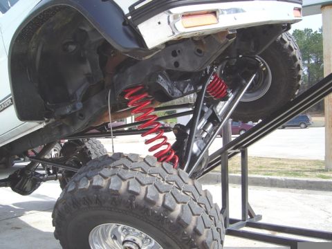 1986 Ford Bronco - Close-up view of a heavily modified SUV's suspension system, showing custom components and large tires.