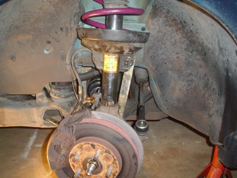 1993 Ford Taurus - Close-up view of a vehicle's front suspension strut, brake rotor, and caliper, with a yellow warning label visible on the strut.