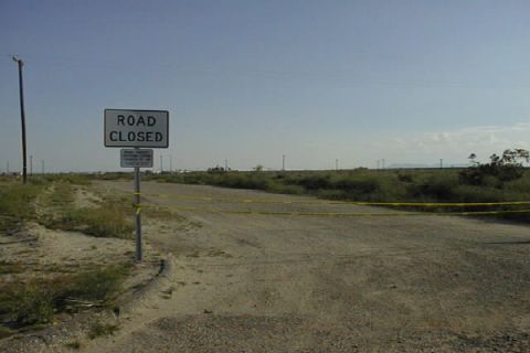 1997 Ford Ranger - A white "ROAD CLOSED" sign on a metal post beside a gravel road, with yellow caution tape strung across the roadway. Power poles, desert sc…