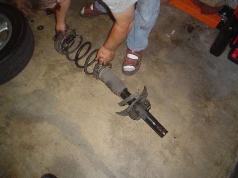 1993 Ford Taurus - A person holds a front strut assembly, likely for a car, as it is being worked on or removed.