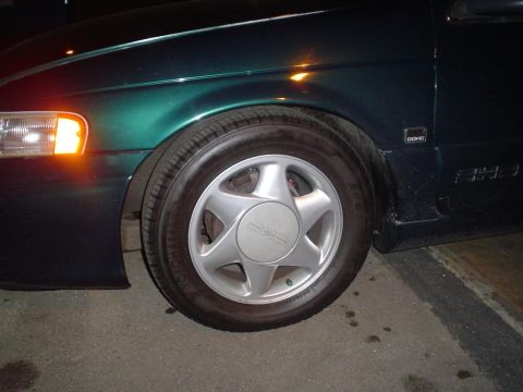1993 Ford Taurus - Close-up of a green car's front wheel and fender, showing a DOHC badge and '8H3' badging.