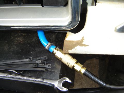 1991 Ford Bronco - Close-up of an air hose fitting and blue tubing attached to a vehicle's exterior, with tools and fasteners visible.