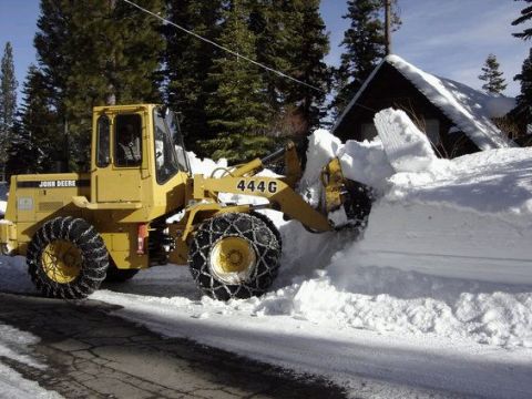1995 Ford Bronco - A yellow John Deere 444G wheel loader equipped with tire chains is actively clearing a large pile of snow from a road.