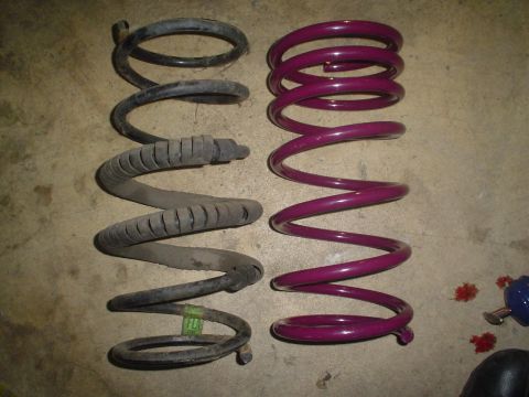 1993 Ford Taurus - A comparison of two coil springs, one in a dark color and the other in a vibrant purple, resting on a concrete surface.