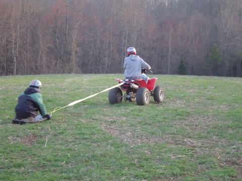 1995 Ford Bronco - A person on a red ATV tows another person on a sled through a grassy field with trees in the background.