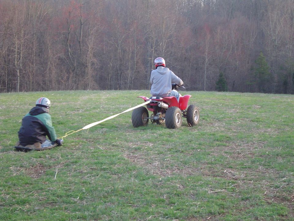 Red ATV towing a person on a sled across a grassy field