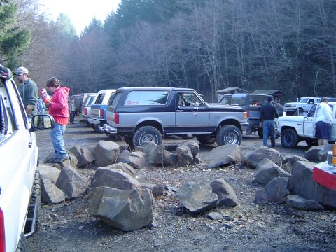 1989 Ford Bronco - A two-tone 1989 Ford Bronco is parked in a lot with other vehicles and large rocks.