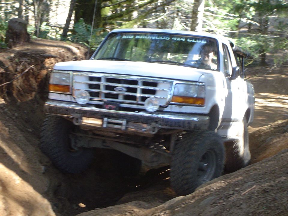 White Ford 4x4 flexing over rutted forest trail, front view with winch bumper